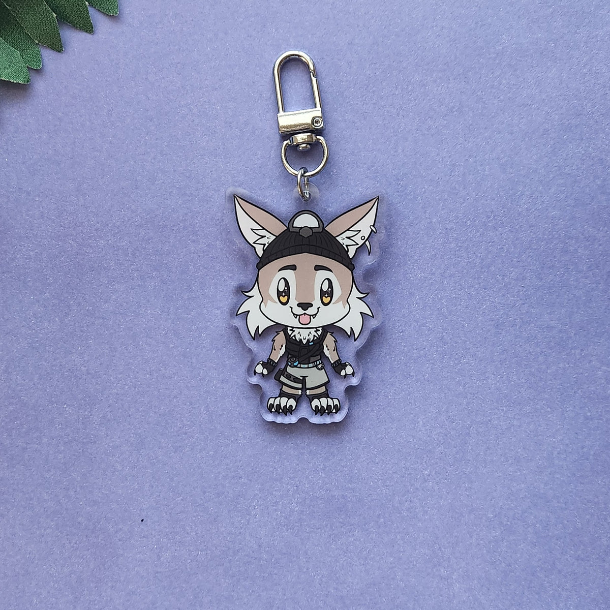 A chibi-style acrylic keychain featuring a cute fox character with large ears, wearing a black and white outfit, attached to a silver metal clasp and photographed on a lavender background.