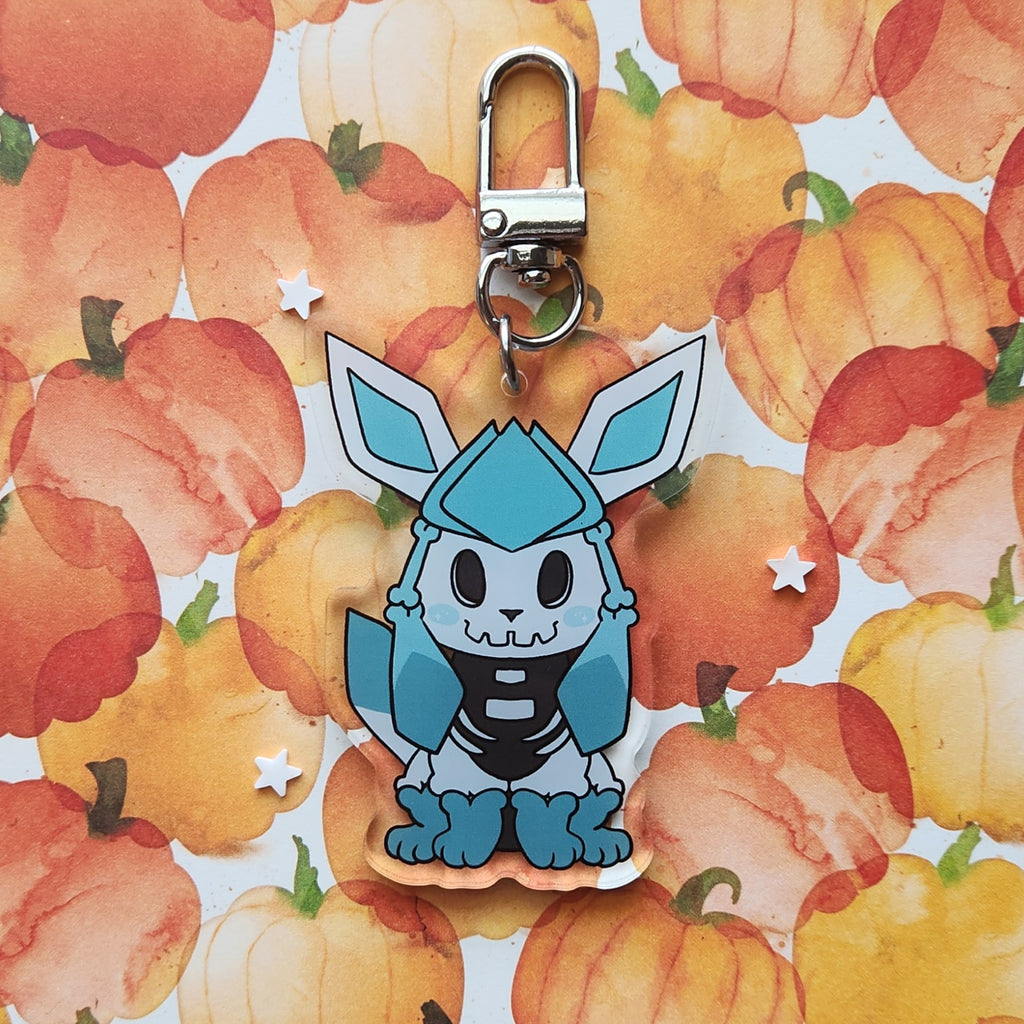 A blue and white skeleton cartoon character keychain charm with a silver lobster clasp, displayed on a watercolor pumpkin patterned background.
