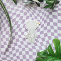 A die-cut sticker featuring a minimalist white cartoon character with a small gold star accent, displayed on a purple and white checkered background with green leaves.