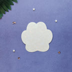 A translucent, paw-shaped acrylic nail art sticker or decal with a subtle iridescent sheen, displayed on a textured purple background with decorative star and leaf props.