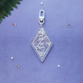 A clear acrylic keychain charm with a silver clasp, featuring a paw print design with glitter and small star details, displayed on a textured purple background with decorative star confetti and a green leaf.