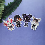 Four die-cut vinyl stickers featuring cute chibi anime-style animal characters, arranged on a textured lavender-blue background with a green fern leaf in the top-left corner.