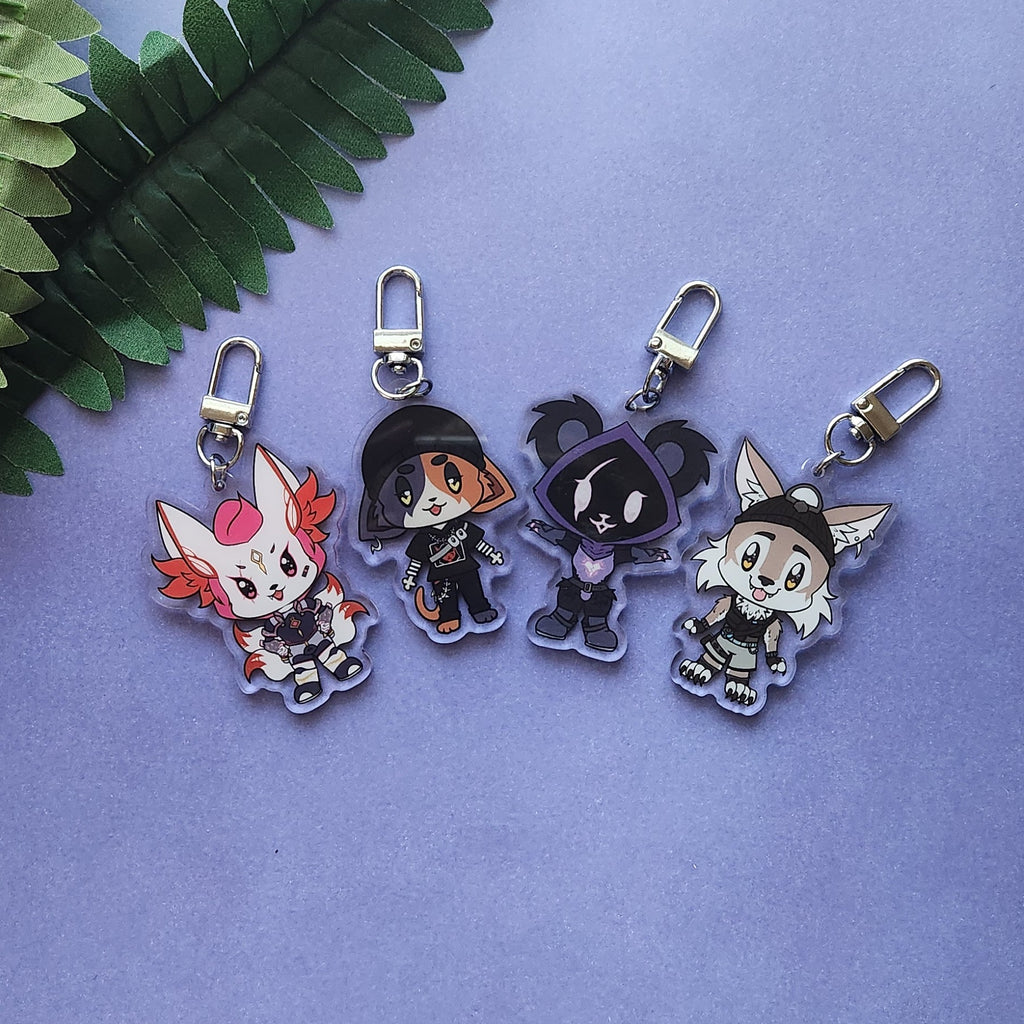 Four chibi anime keychains with silver lobster clasps, arranged on a lavender background with a green fern leaf in the top left corner.