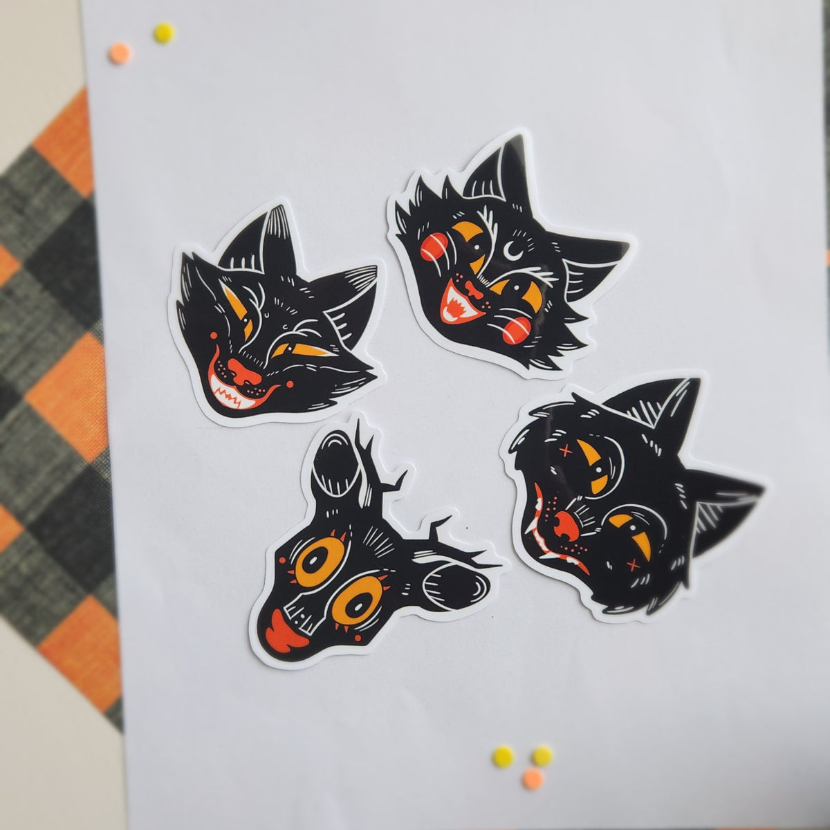 Four die-cut vinyl stickers featuring stylized black animal heads with orange and yellow eyes and red accents, arranged on a white sheet of paper.