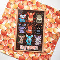 A rectangular Halloween greeting card featuring cute cartoon foxes on a dark brown background with the words 'STAY SPOOKY!' at the bottom, placed on top of a pumpkin-patterned sheet.