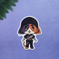 A die-cut sticker featuring a chibi-style cartoon cat character wearing a black cap, black outfit, and holding a small knife, placed on a textured purple surface with green leaves in the top-left corner.
