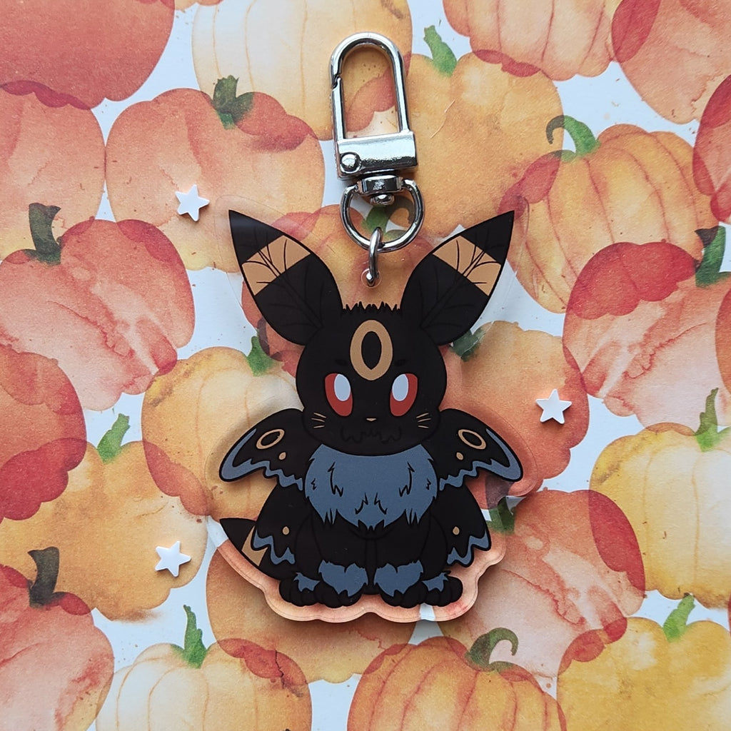 A black moth fox keychain charm with a silver lobster clasp, displayed on a watercolor pumpkin patterned background.