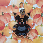 A black moth fox keychain charm with a silver lobster clasp, displayed on a watercolor pumpkin patterned background.