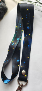 A black  lanyard strap featuring a colorful floral print with white flowers, finished with a silver metal snap button and a gold-tone split ring.