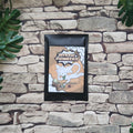 A black-framed art print featuring a cartoon white cat and the text 'MYSTIC PIONEERS' is mounted on a rustic stone wall with green leaves in the corners.