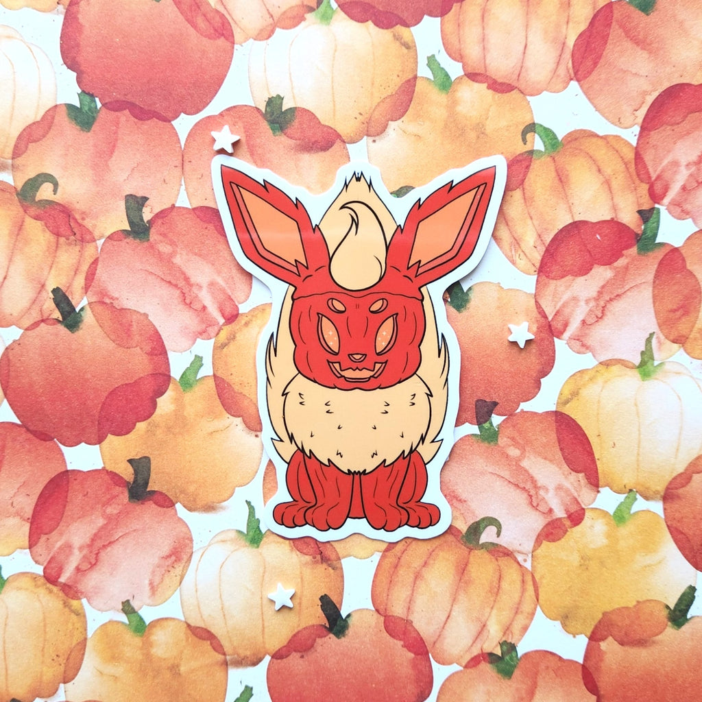 A die-cut sticker featuring a pumpkin fox, centered on a background of watercolor pumpkins in shades of orange, red, and yellow.