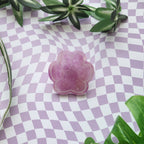 A pink paw-shaped resin charm with glittery purple inclusions, displayed on a lavender and white checkered background with green leaves.