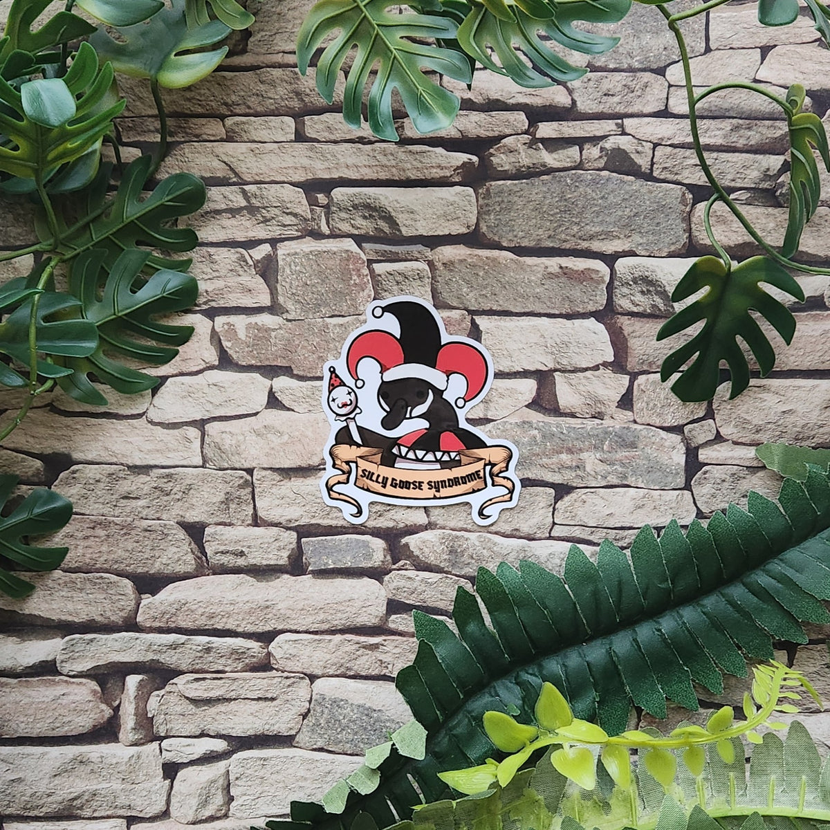 A die-cut sticker featuring a stylized jester goose with the text 'silly goose syndrome' on a banner, placed against a faux stone wall backdrop with green leaves.