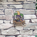 A pin featuring a cartoon goose in a jester hat with the text 'silly goose syndrome', laid on a stone backdrop.