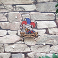A pin featuring a cartoon goose in a jester hat with the text 'silly goose syndrome', laid on a stone backdrop.