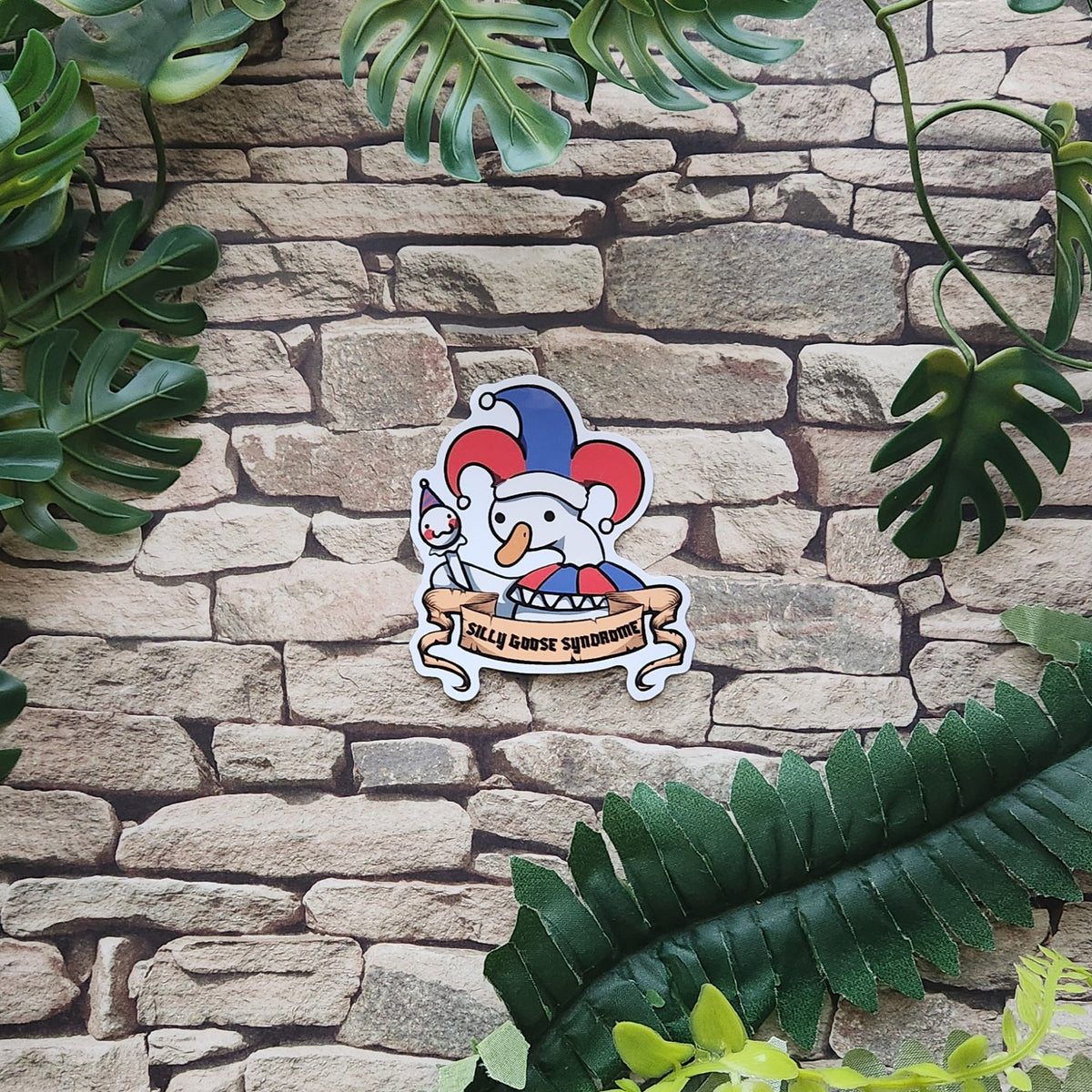 A die-cut sticker featuring a cartoon goose dressed as a jester with the text 'SILLY GOOSE SYNDROME' on a banner, displayed on a stone wall with green tropical leaves.