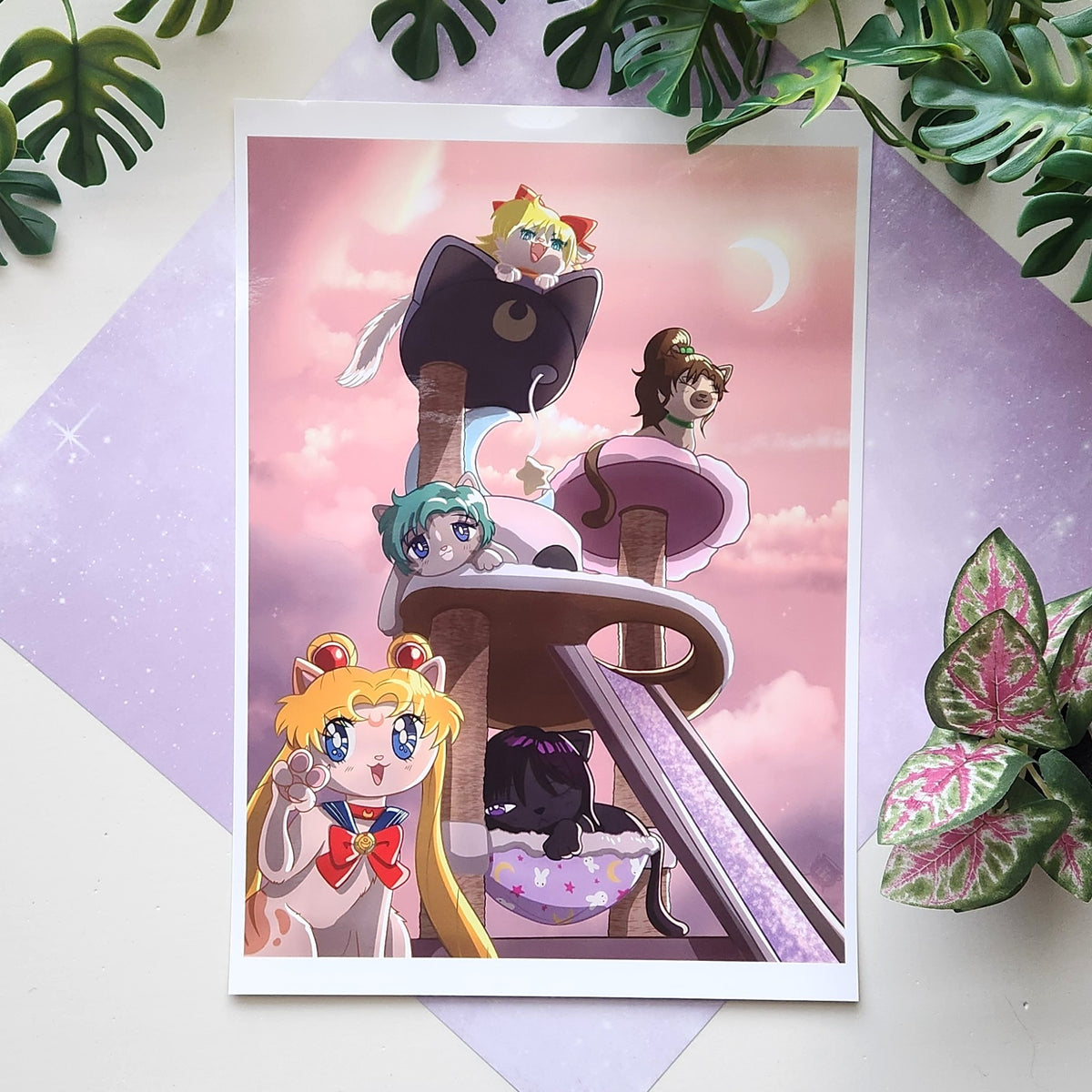 A printed anime art card featuring cat-themed characters on a cat tree, styled on a pastel purple background with green plant leaves around it.