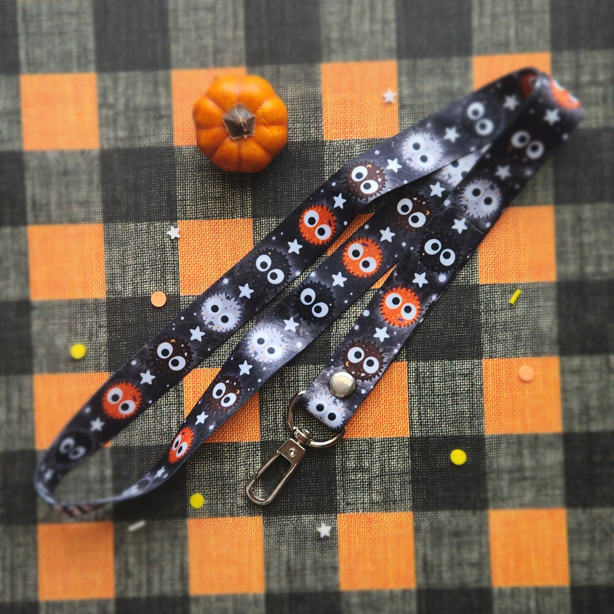 A Halloween-themed lanyard with a black background and cute balls. It features a silver metal lobster clasp at one end.